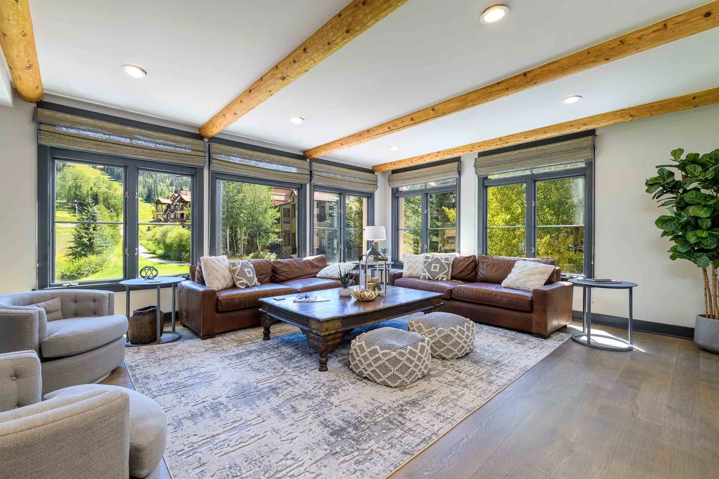 A bright living room with sectional seating and large windows overlooking greenery.