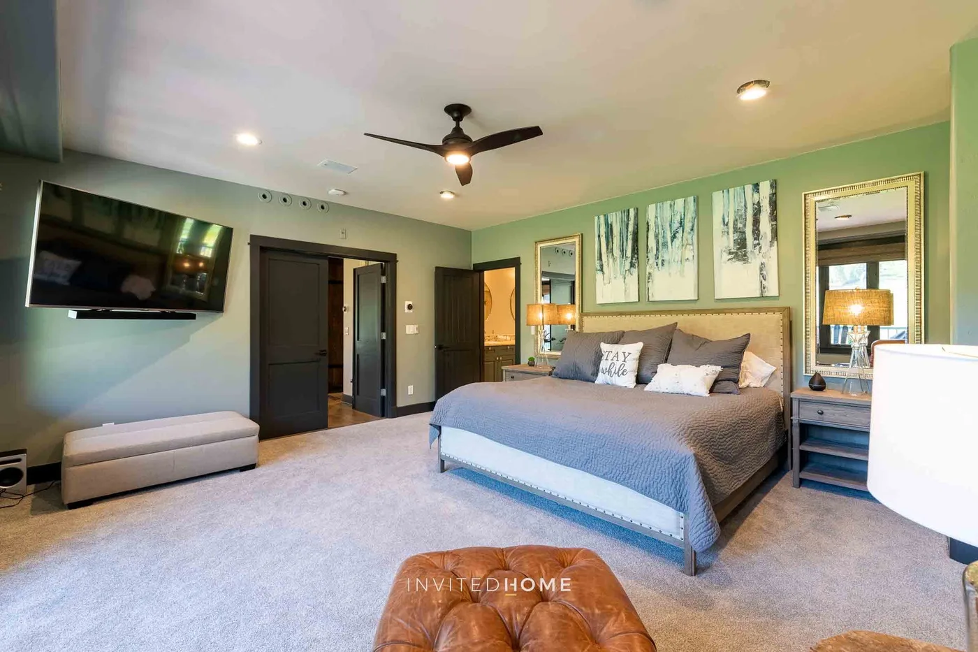 A bedroom with a large bed, wall-mounted television, and ceiling fan.