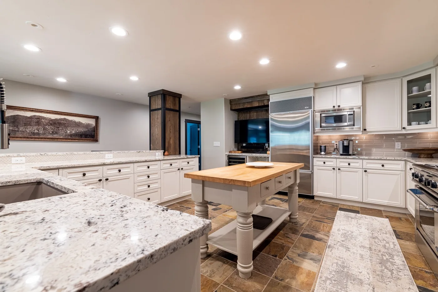 A bright kitchen with white cabinetry, stone counters, and a central island.