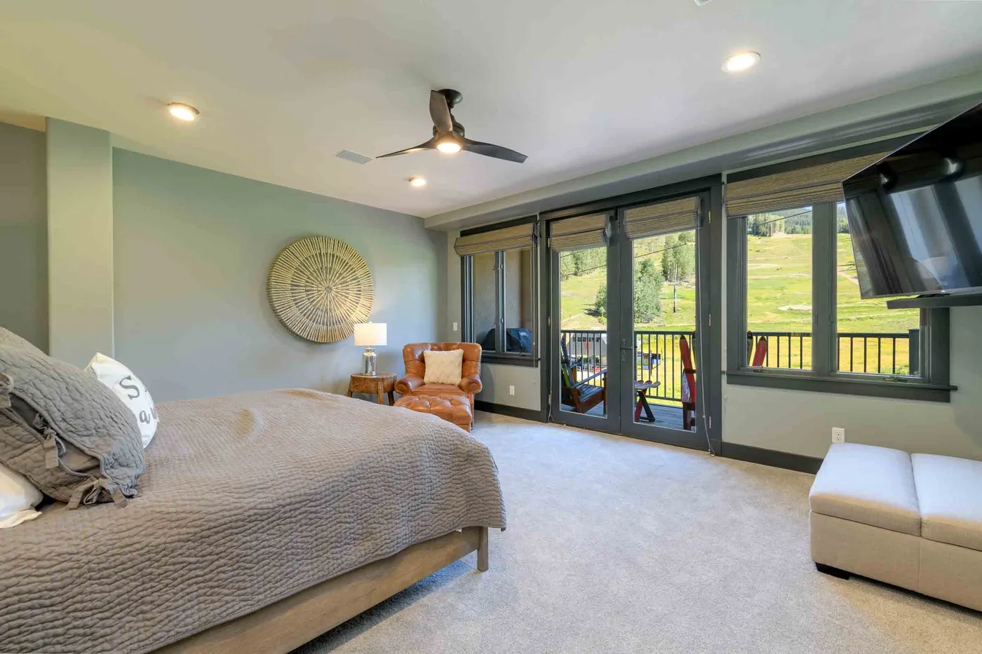 A bedroom with a bed, seating, and large windows overlooking a green hillside.