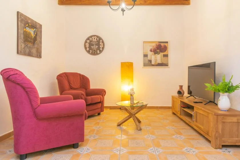 A living room with colorful seating, a television, and a low wooden cabinet.