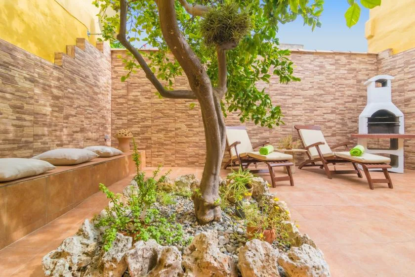 An outdoor patio with a tree, lounge seating, and a built-in barbecue.