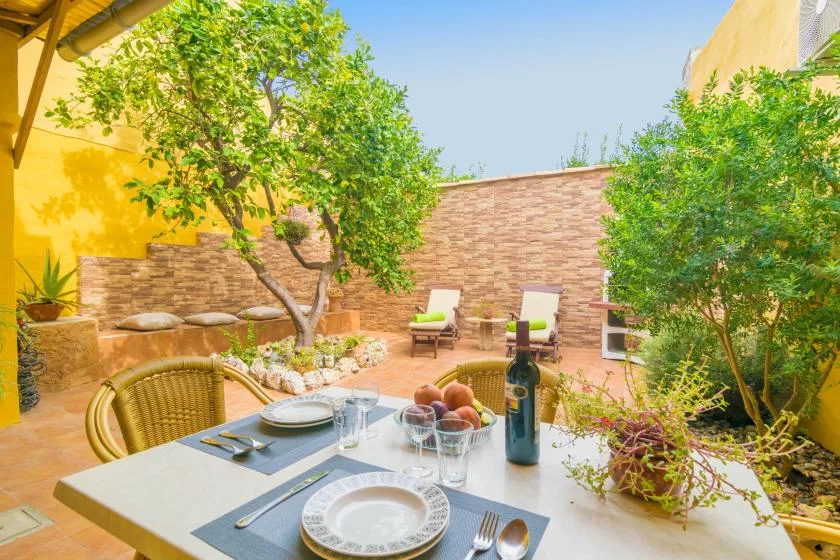 An outdoor dining area with a table set beneath leafy trees.