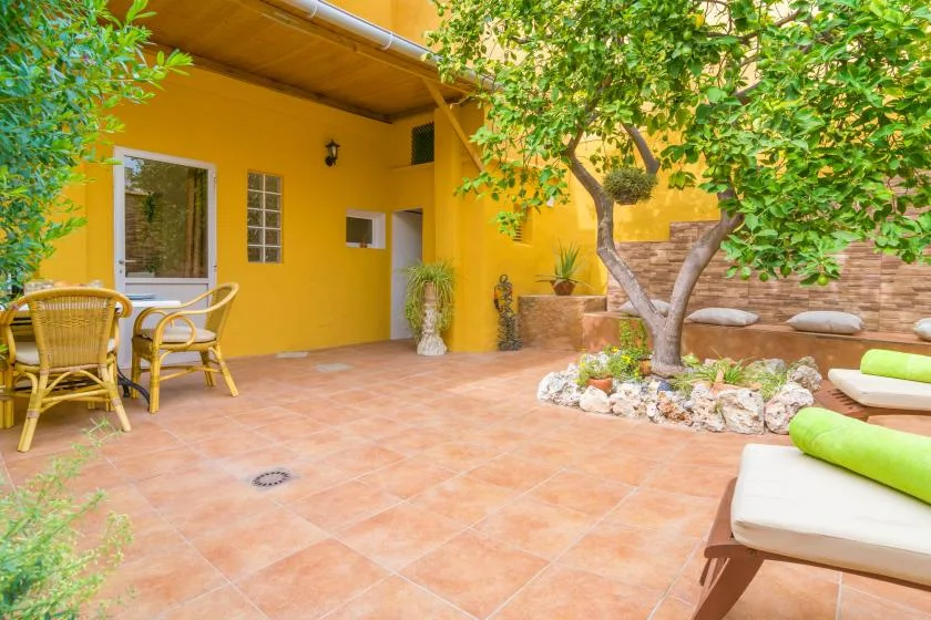 A sunny tiled patio with outdoor seating and a leafy tree.