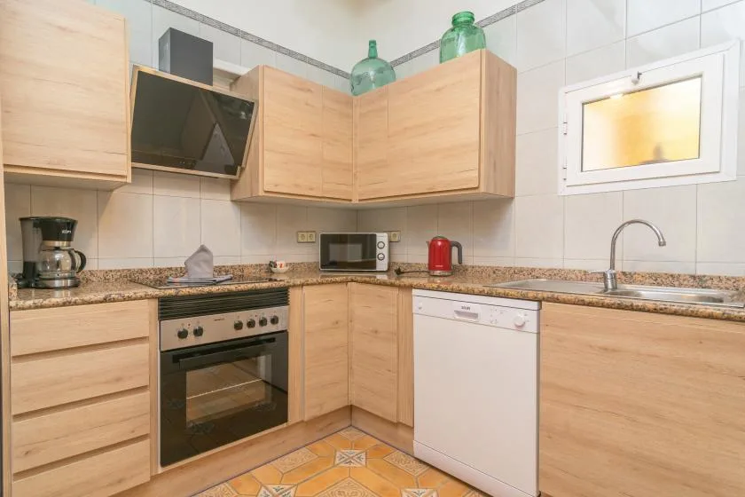 A bright tiled kitchen with light wood cabinets, a countertop, and built-in appliances.