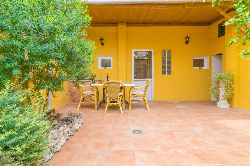 A covered outdoor patio with a dining table and seating beside a bright yellow wall.