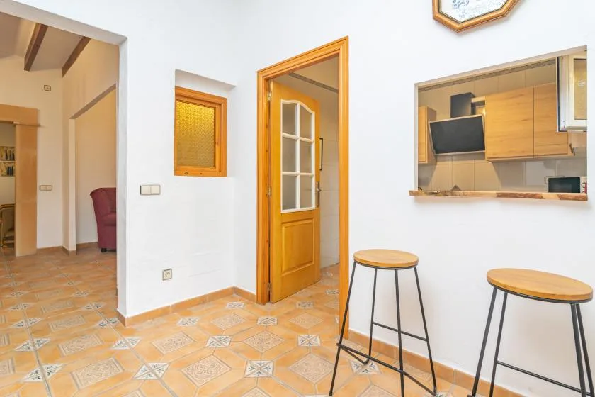 A bright interior shows a tiled floor, a wooden doorway, and a kitchen counter.