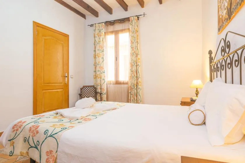 A bedroom with a bed, floral curtains, and exposed ceiling beams.