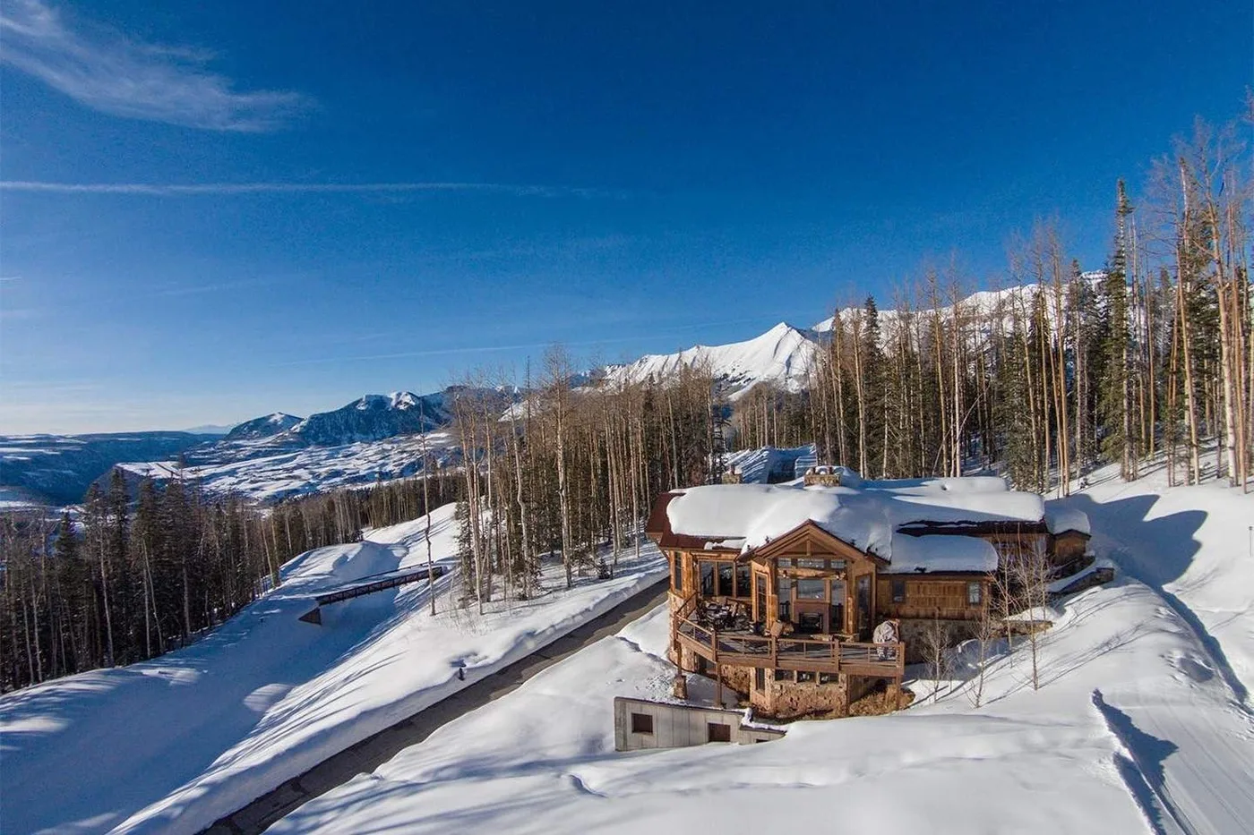 A mountain lodge sits amid snowy slopes and a forest of tall trees.
