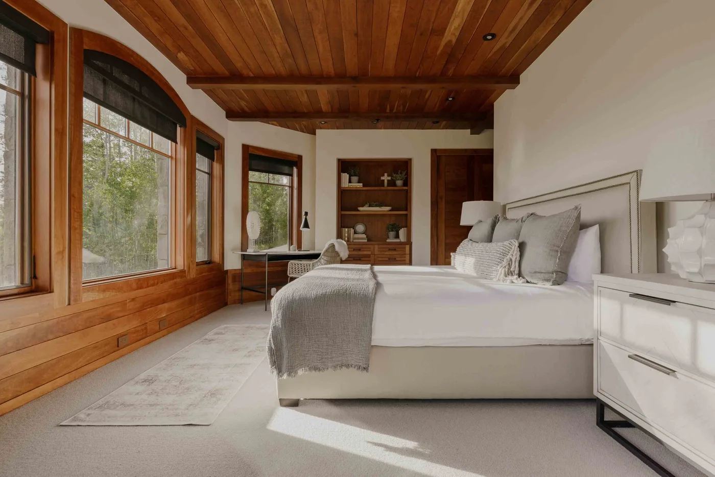 A bedroom with a large bed, wood ceiling, and tall windows.