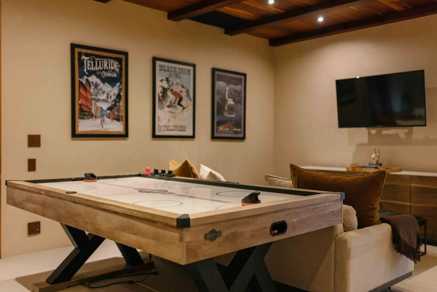 A game room with a shuffleboard table, seating, and a wall-mounted television.