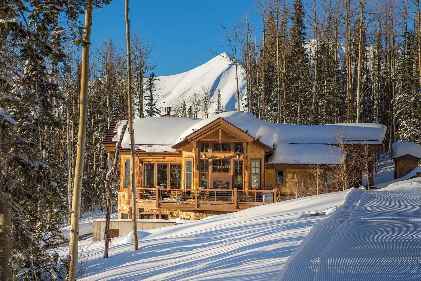 A wooden cabin sits among snowy trees, with a mountain rising behind it.
