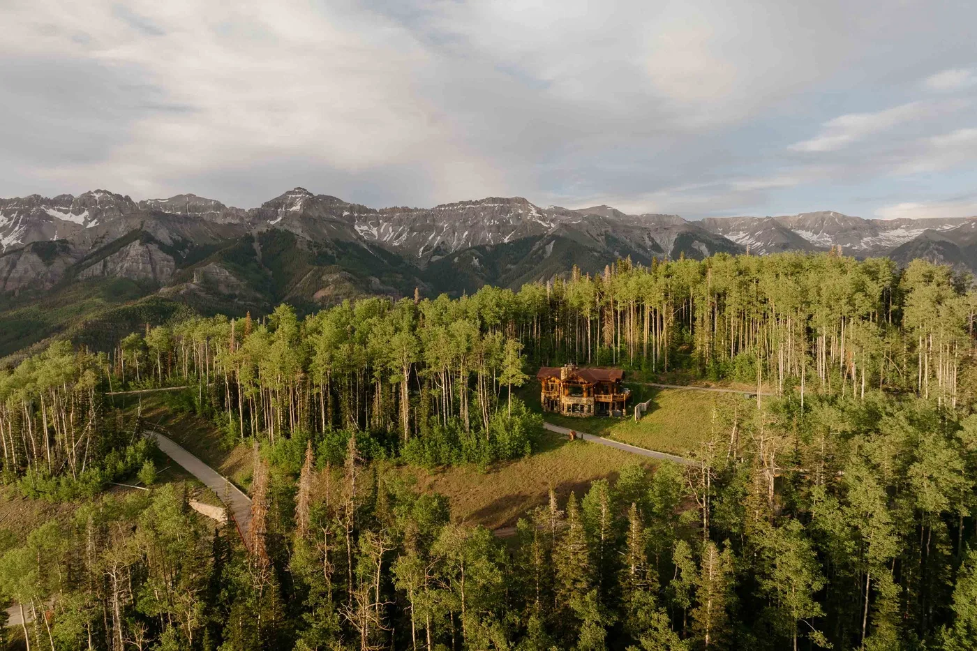 A forested mountain landscape with a small cabin and winding road.