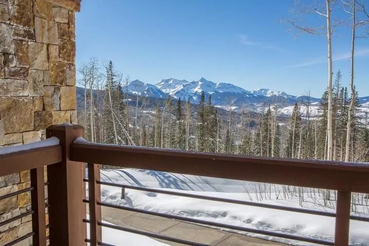 A balcony overlooks a snowy mountain landscape and a stand of trees.