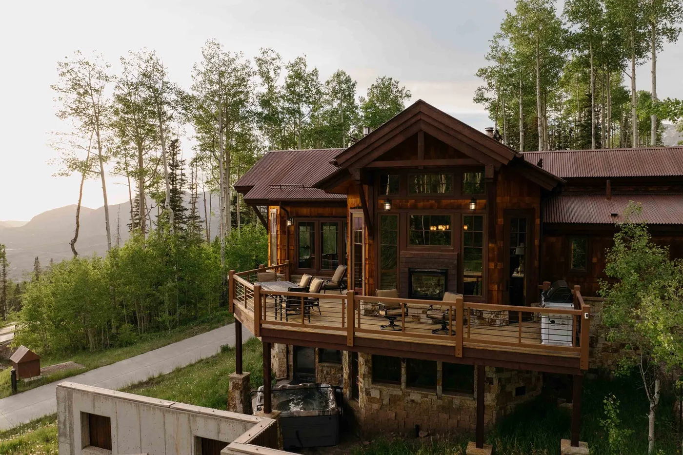 A timber lodge with a spacious outdoor deck sits among trees overlooking a mountain landscape.