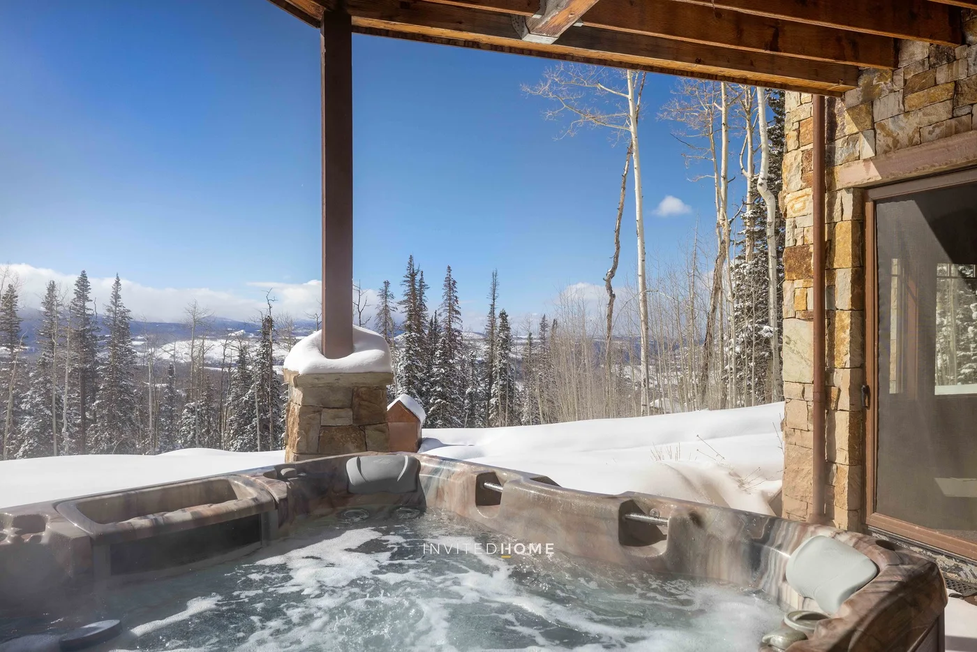 A bubbling outdoor hot tub sits beneath a covered patio overlooking a snowy forest.