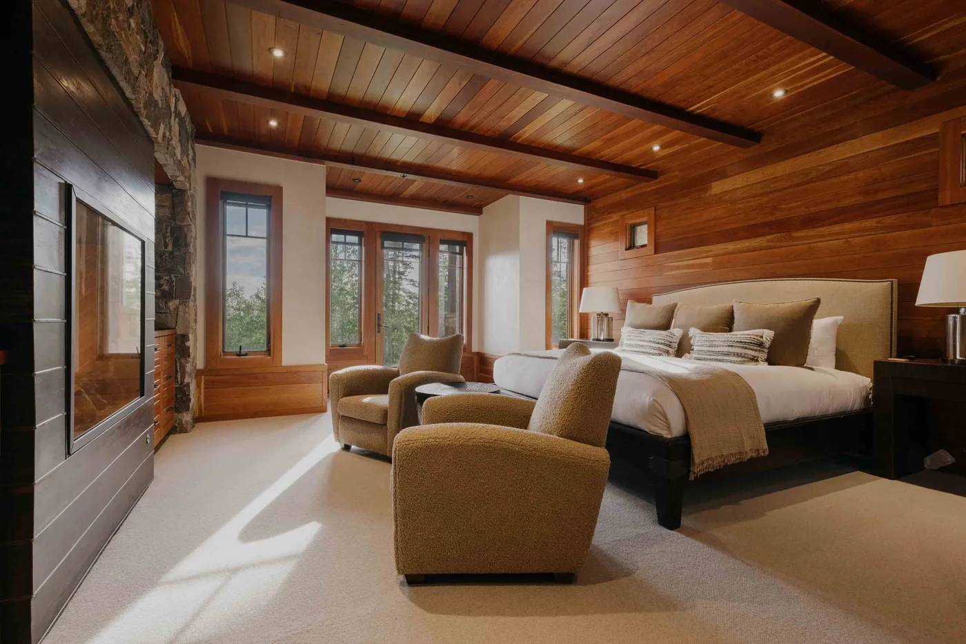 A bedroom with a large bed and upholstered seating beneath a wood-paneled ceiling.