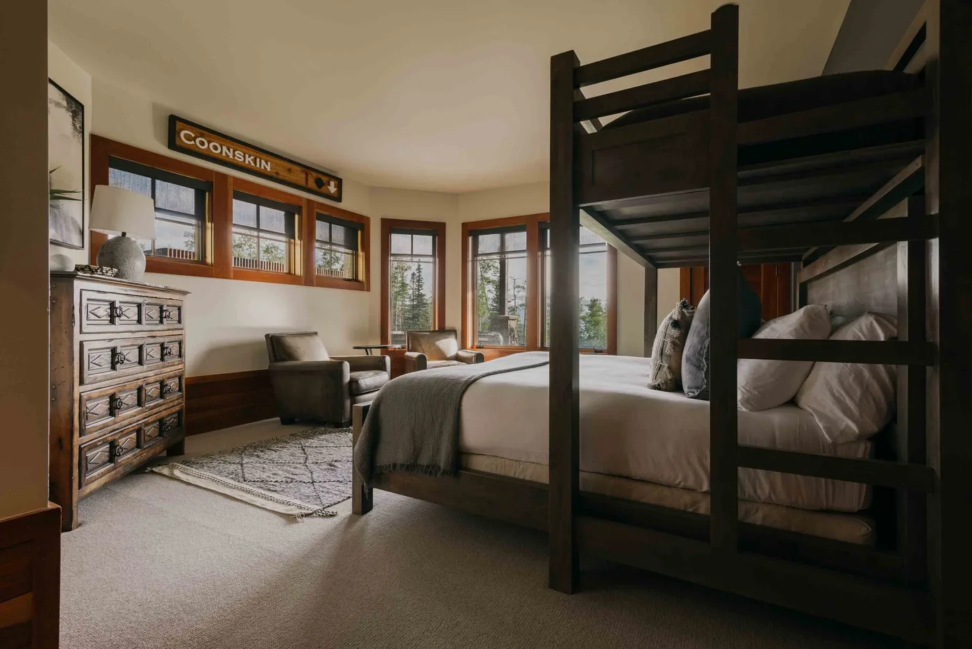 A bedroom with bunk beds, a dresser, and windows overlooking greenery.
