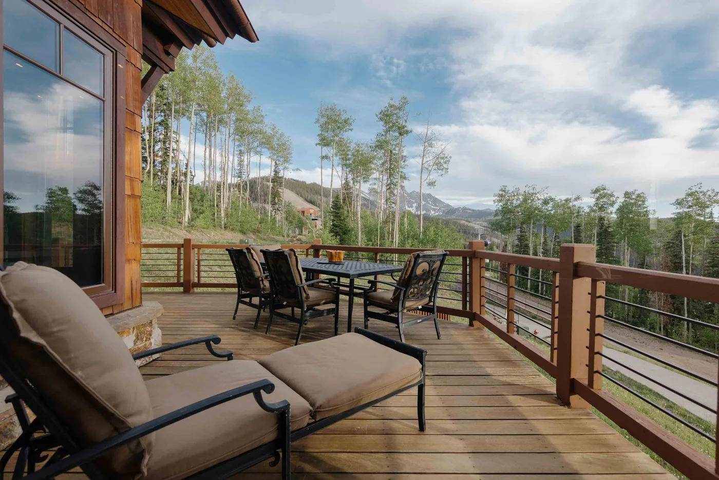 An outdoor deck has seating and a dining table overlooking trees and distant mountains.