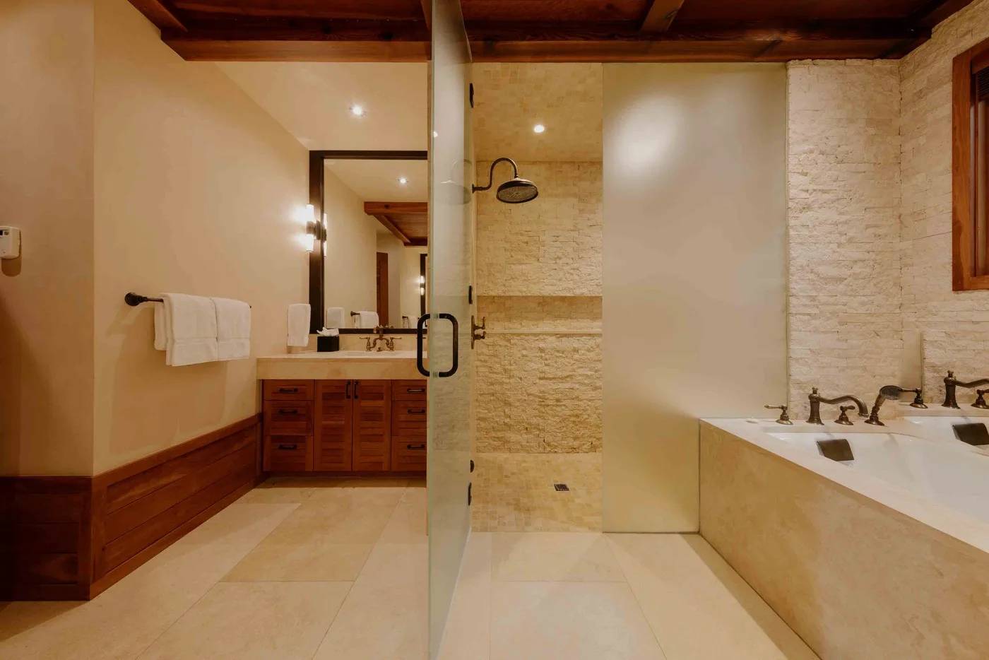 A spacious bathroom with a glass shower partition and a bathtub.