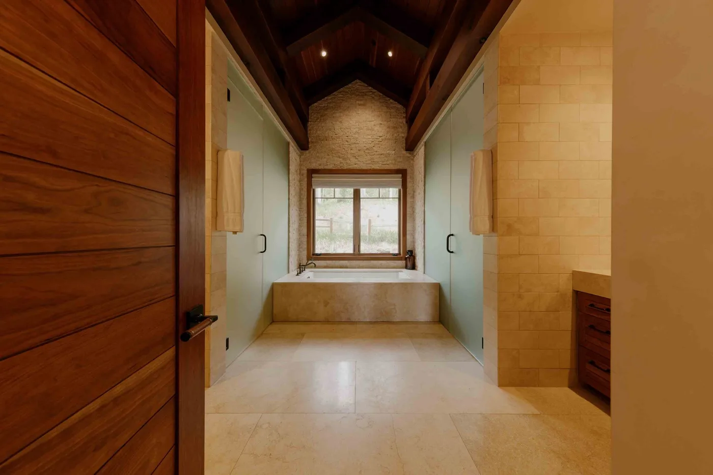 A spacious bathroom with a bathtub beneath a window and a high wood ceiling.