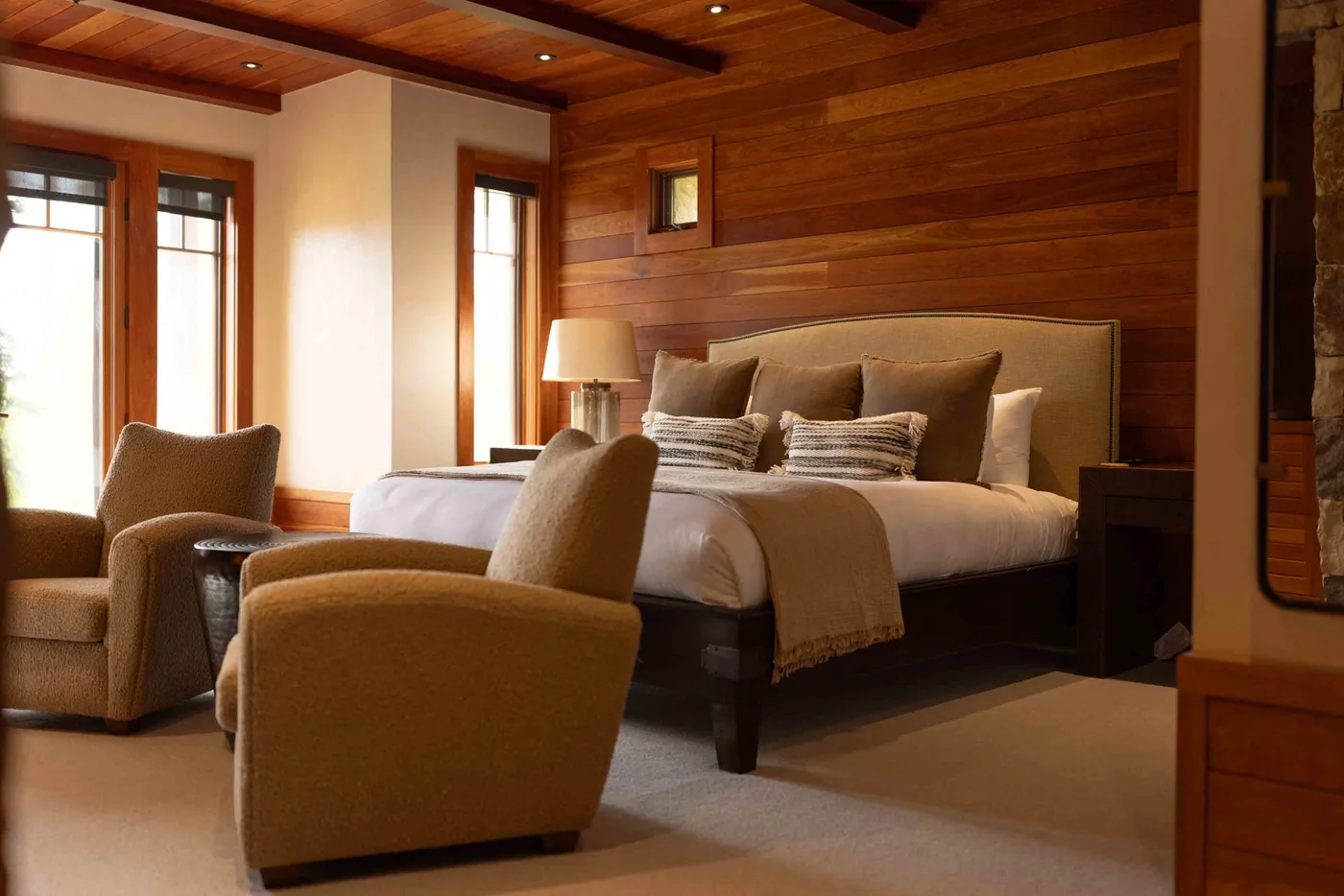 A bedroom with a large bed and upholstered seating beside tall windows.