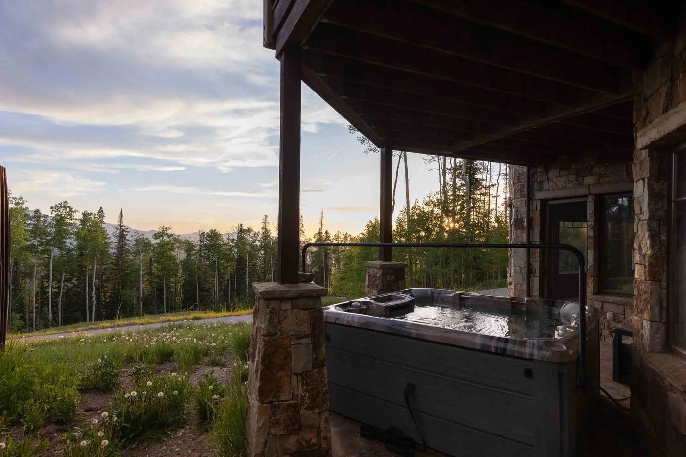 A covered outdoor hot tub overlooks a forest beneath a cloudy evening sky.