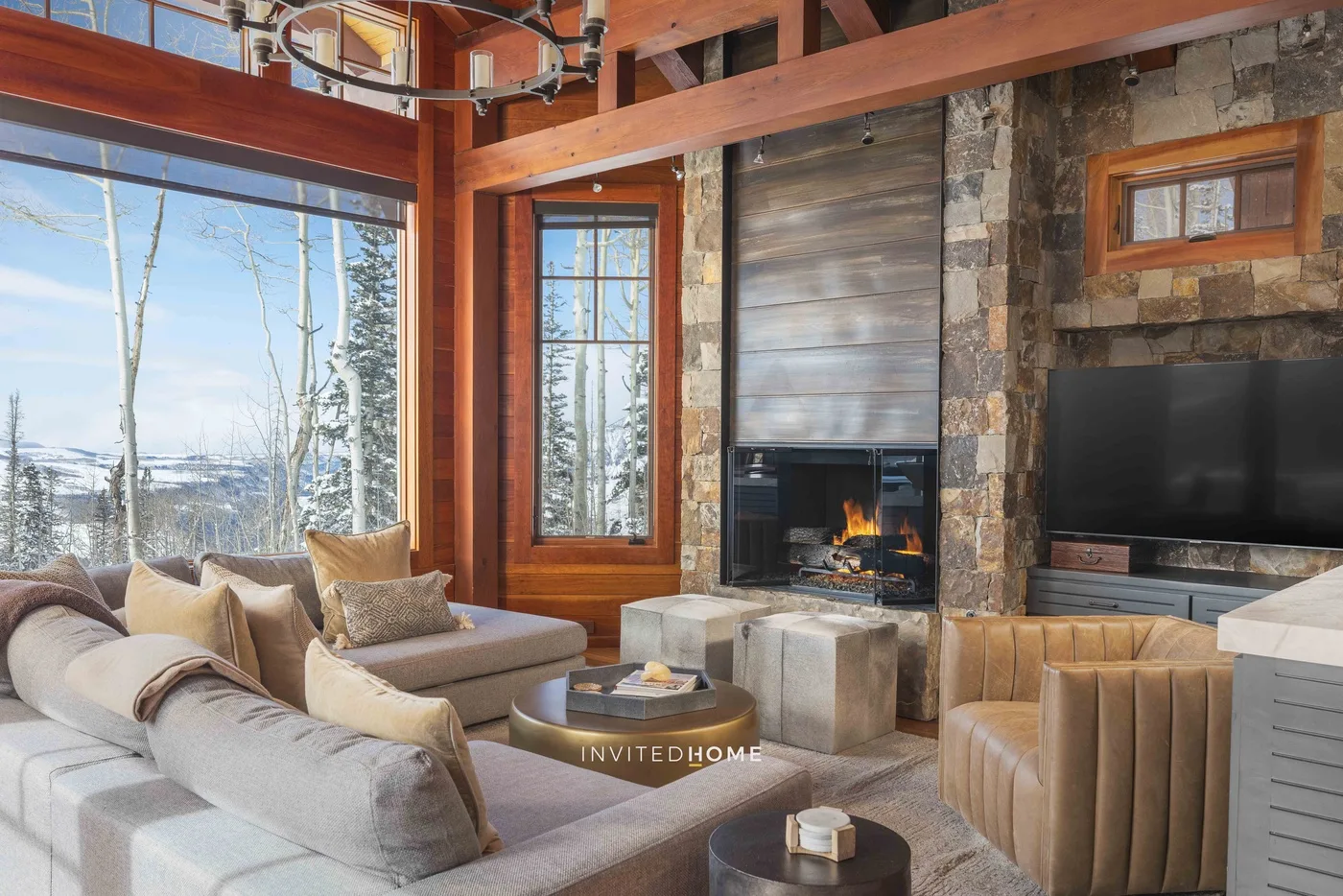 A living room with large windows, a stone fireplace, and seating around a coffee table.