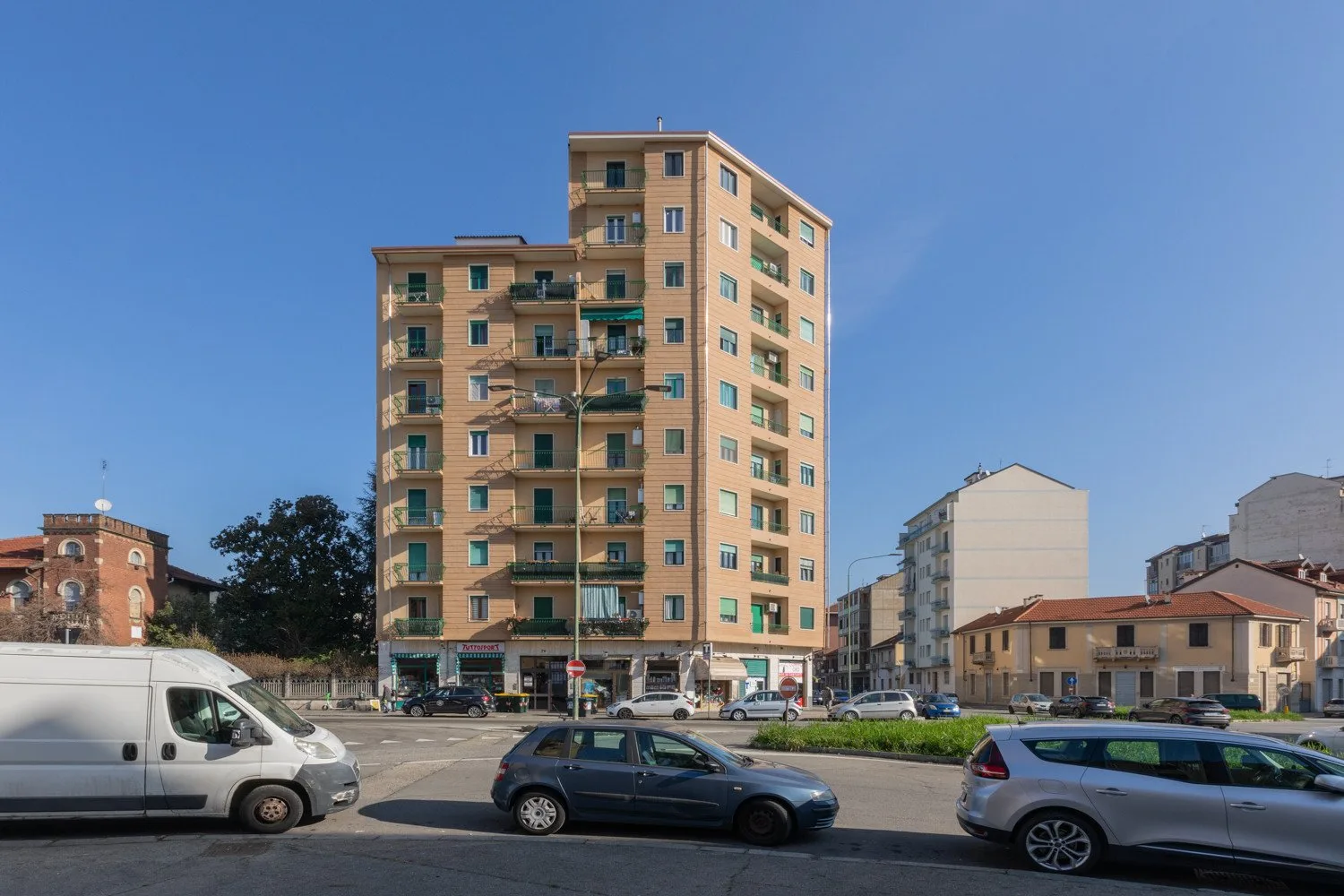 A tall apartment building stands beside a street with parked cars.