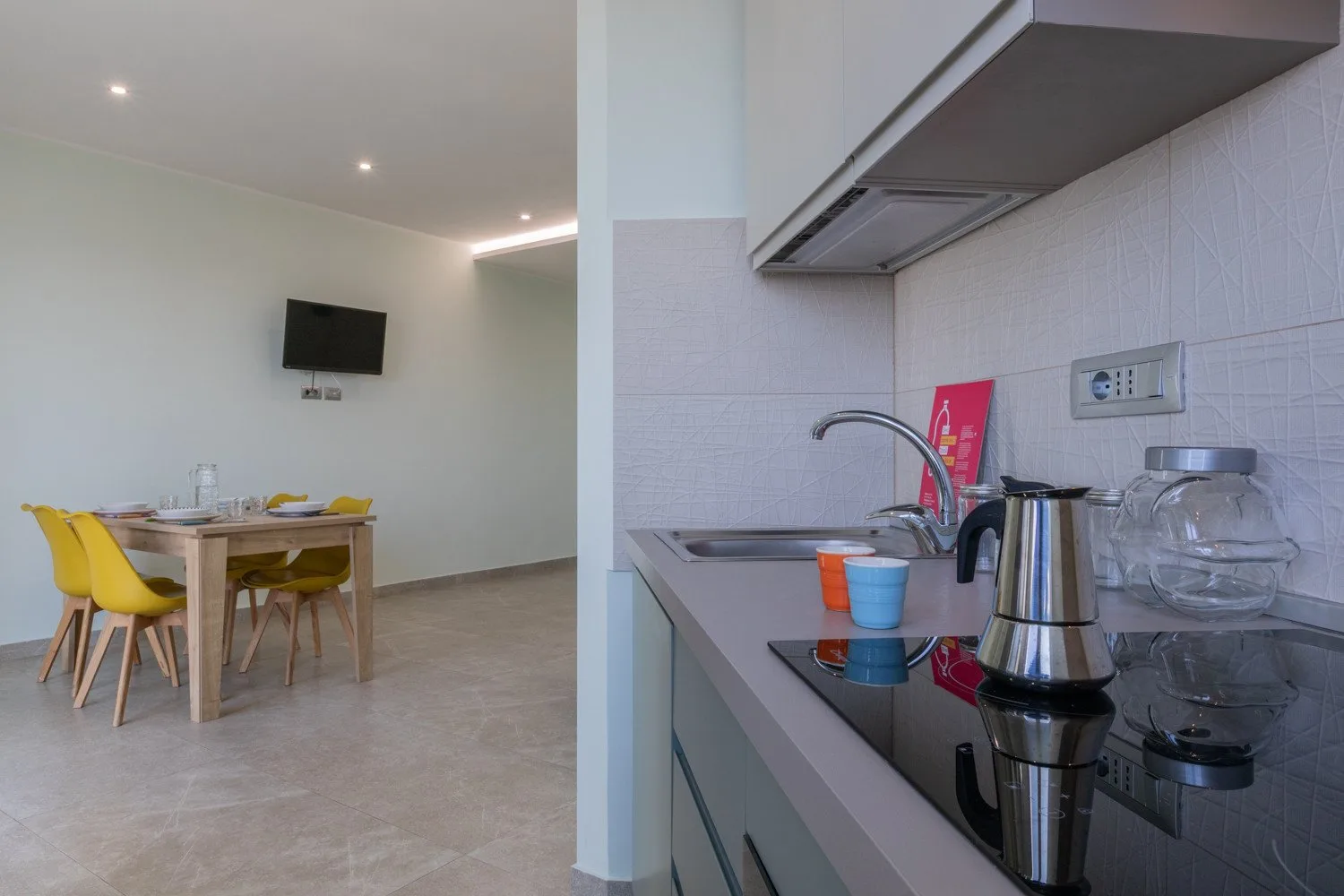 A dining area beside a compact kitchen, with a table and yellow seating.