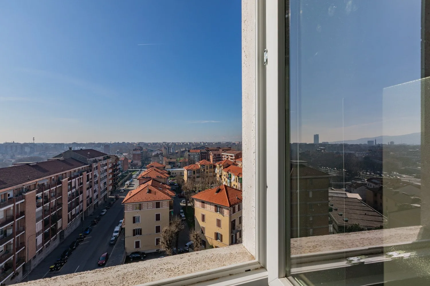 A city view through a window, with buildings and rooftops under a clear sky.