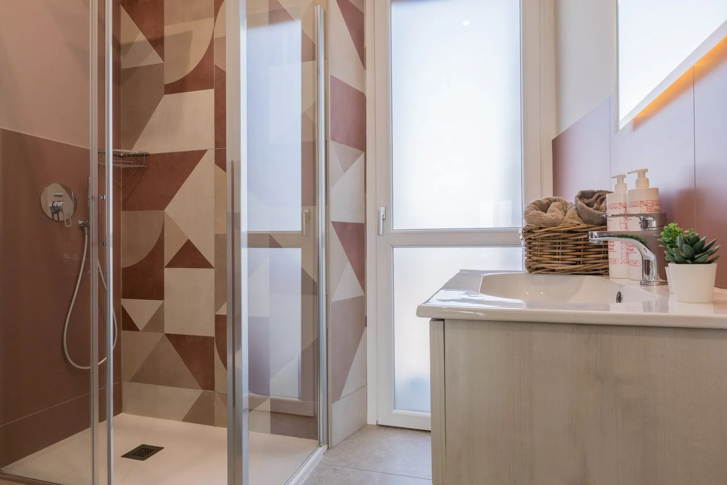 A bathroom with a glass shower and a sink beneath a bright window.
