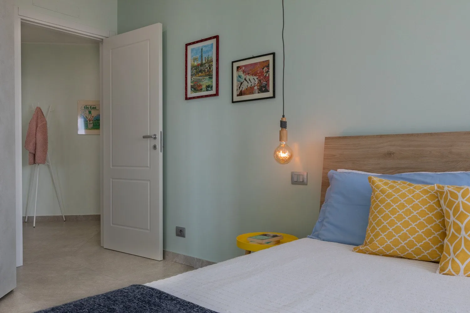 A bedroom with a bed, colorful pillows, and framed pictures on the wall.