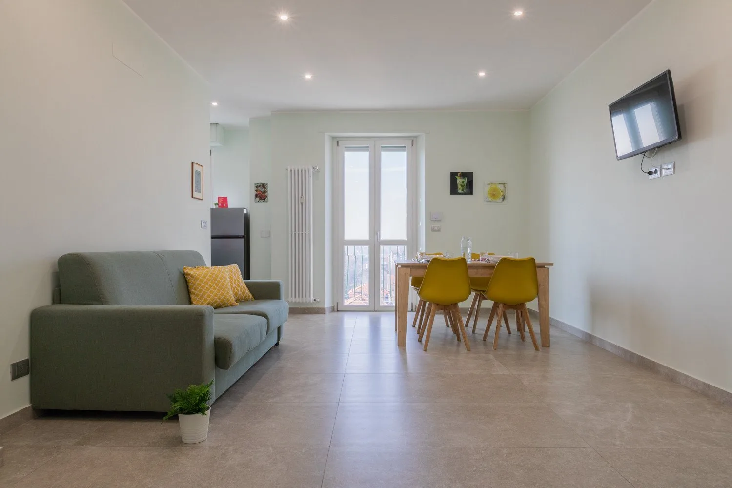 A bright living and dining area with seating, a table, and a wall-mounted television.