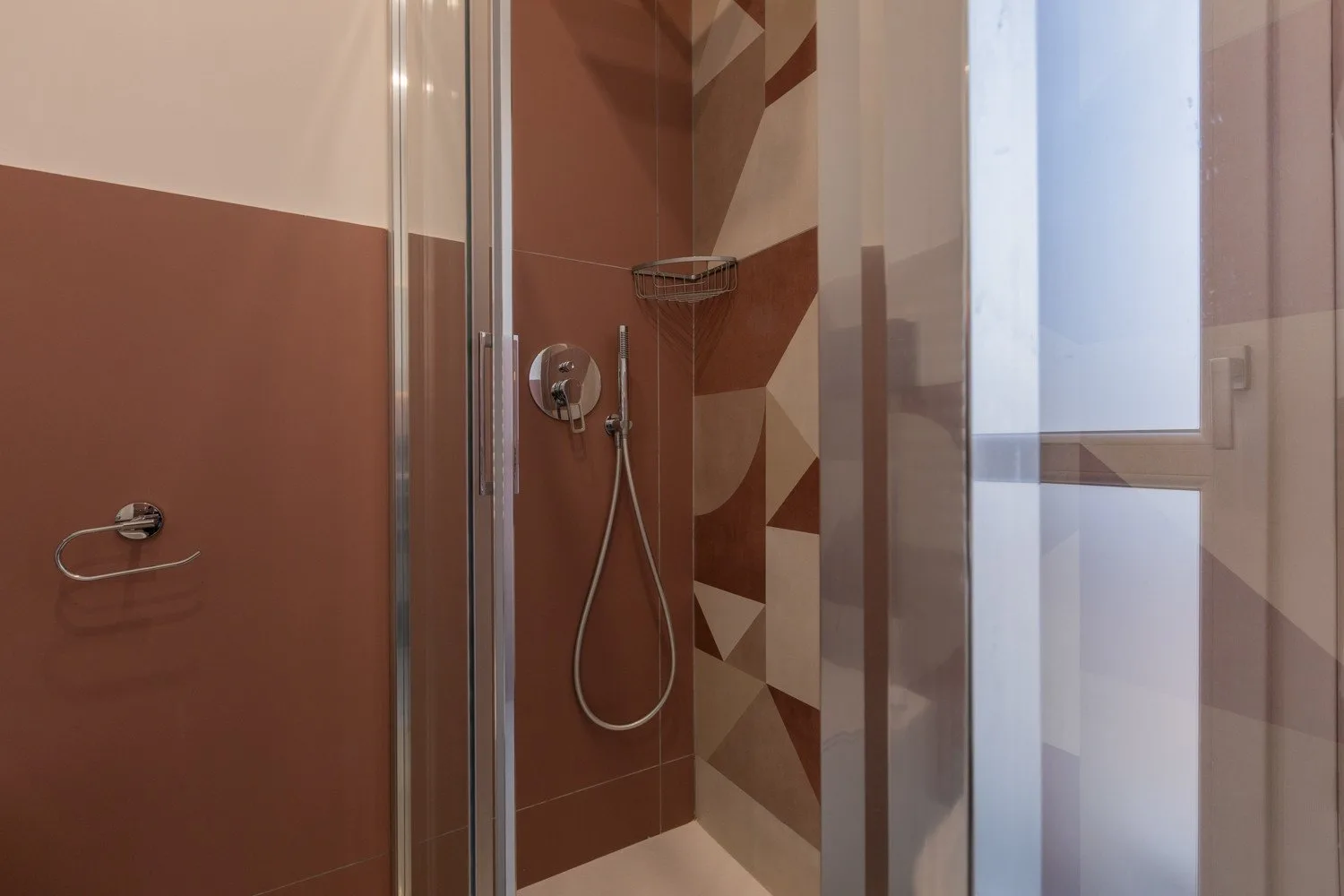 A tiled shower area with a handheld showerhead and glass panels.