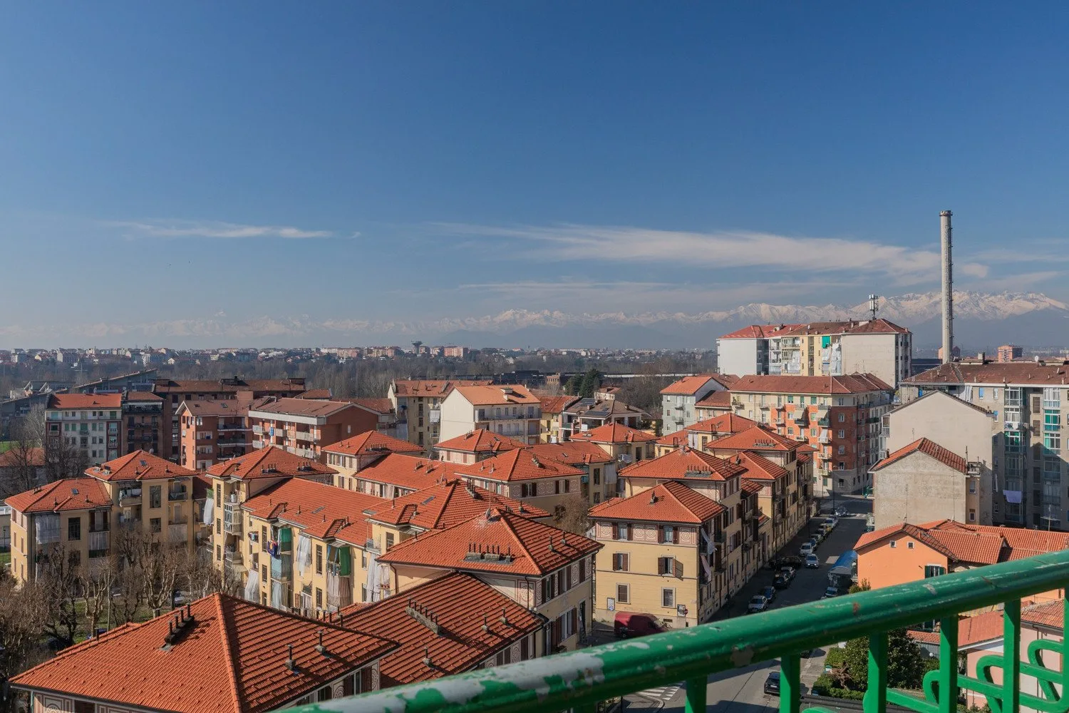 An urban neighborhood of red-roofed buildings sits beneath distant snow-capped mountains.