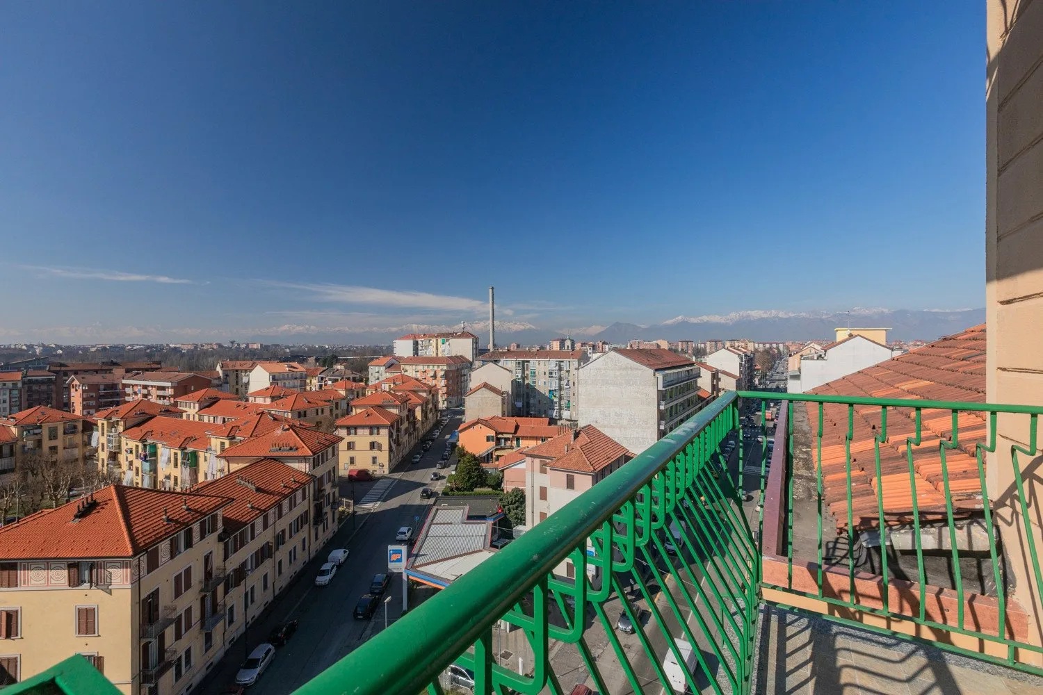 A balcony overlooks a city neighborhood with red-tiled rooftops under a clear sky.