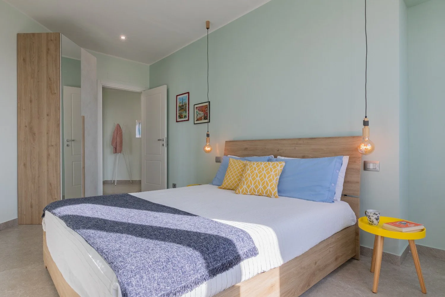 A bedroom with a large bed, colorful pillows, and hanging pendant lights.