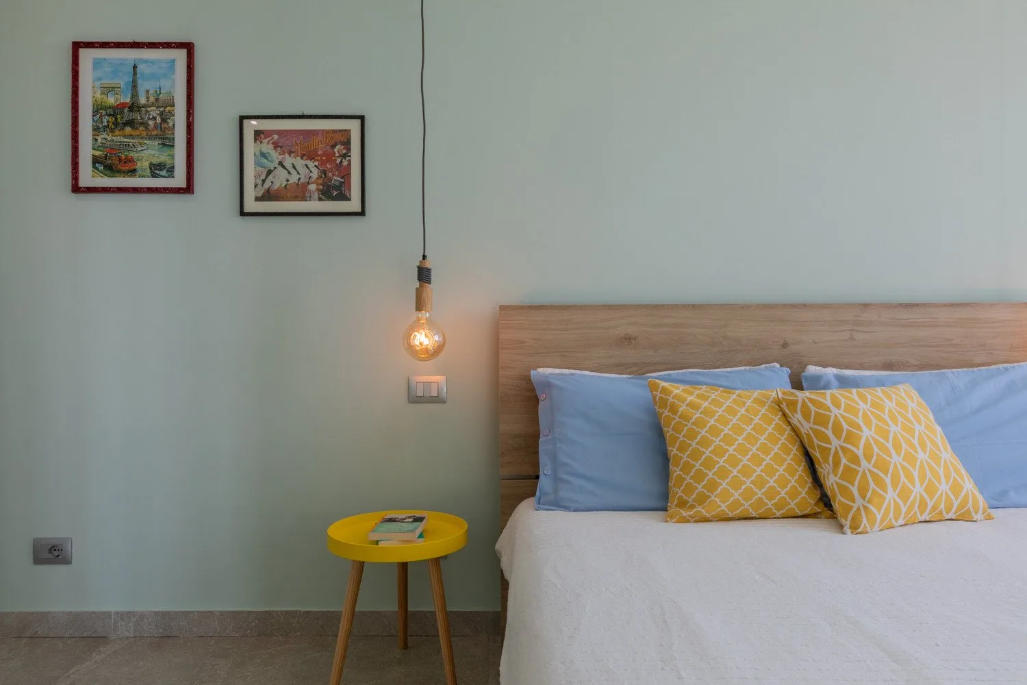 A bedroom with a bed, yellow cushions, and a small bedside table.