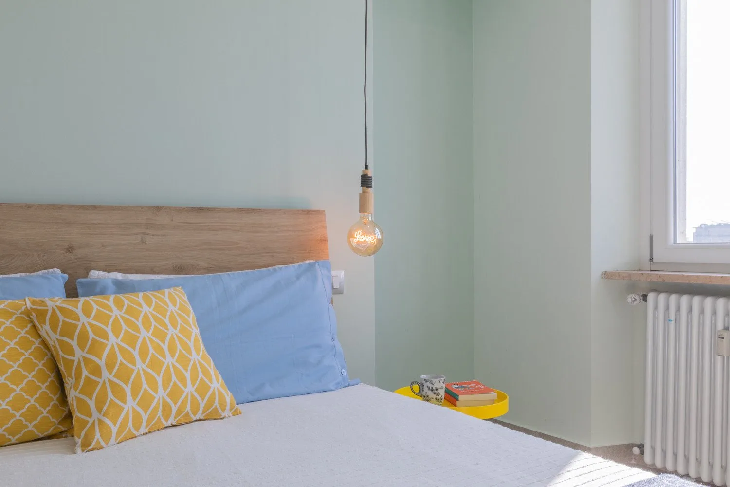 A bedroom with a bed, yellow patterned pillows, and a bedside table.