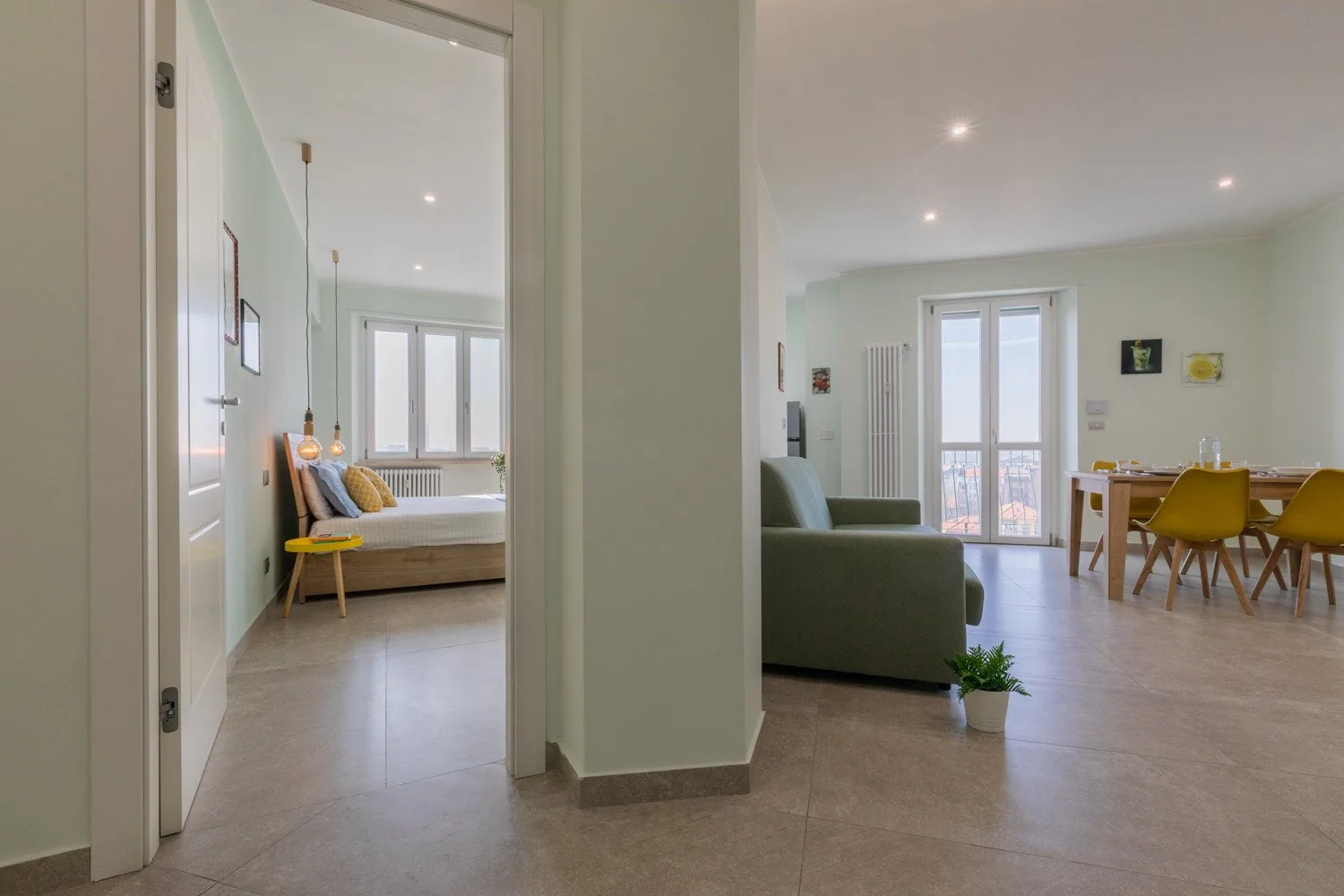 An open-plan living and dining area with a sofa, dining table, and balcony doors.