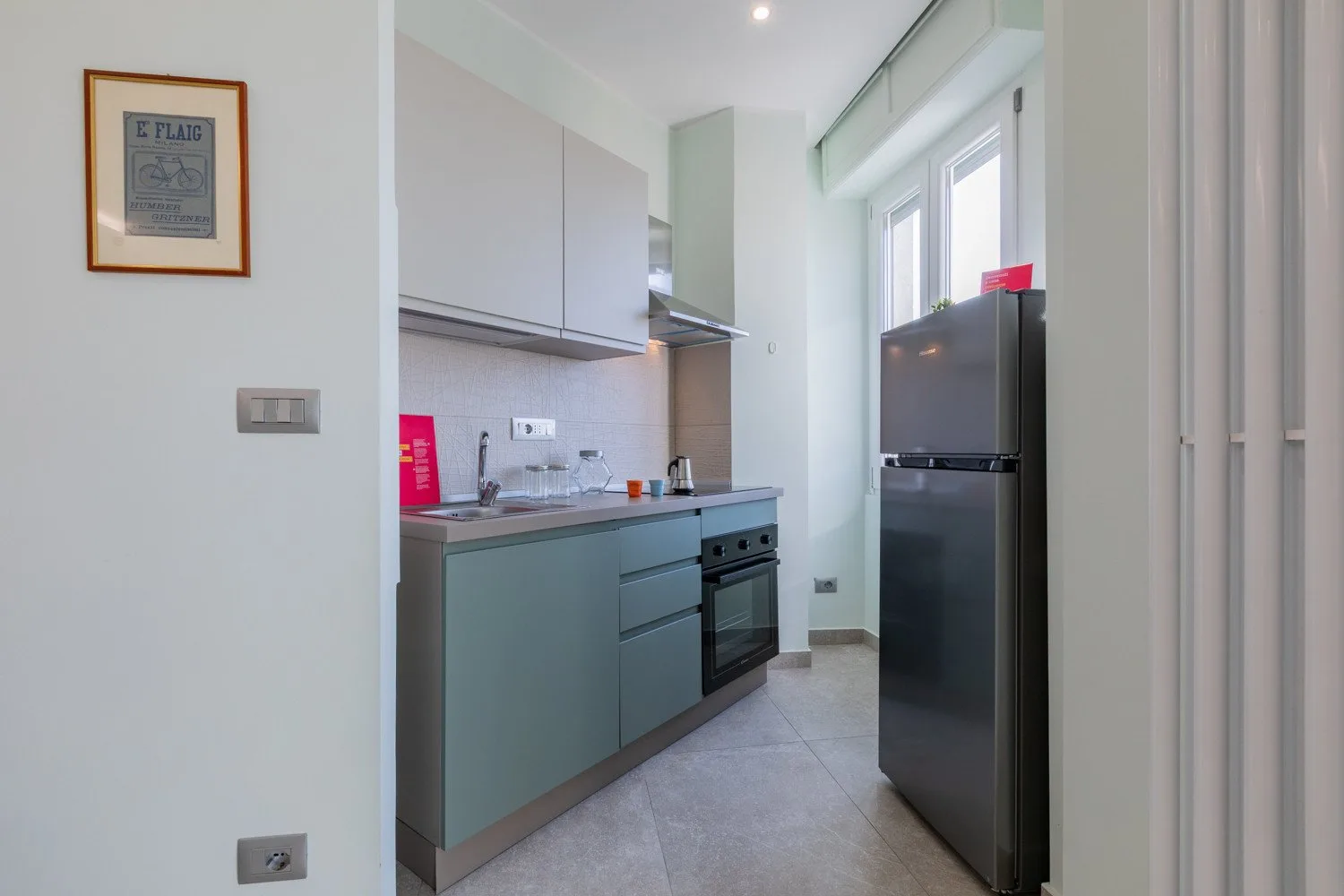 A compact kitchen with cabinets, a countertop, and a refrigerator.