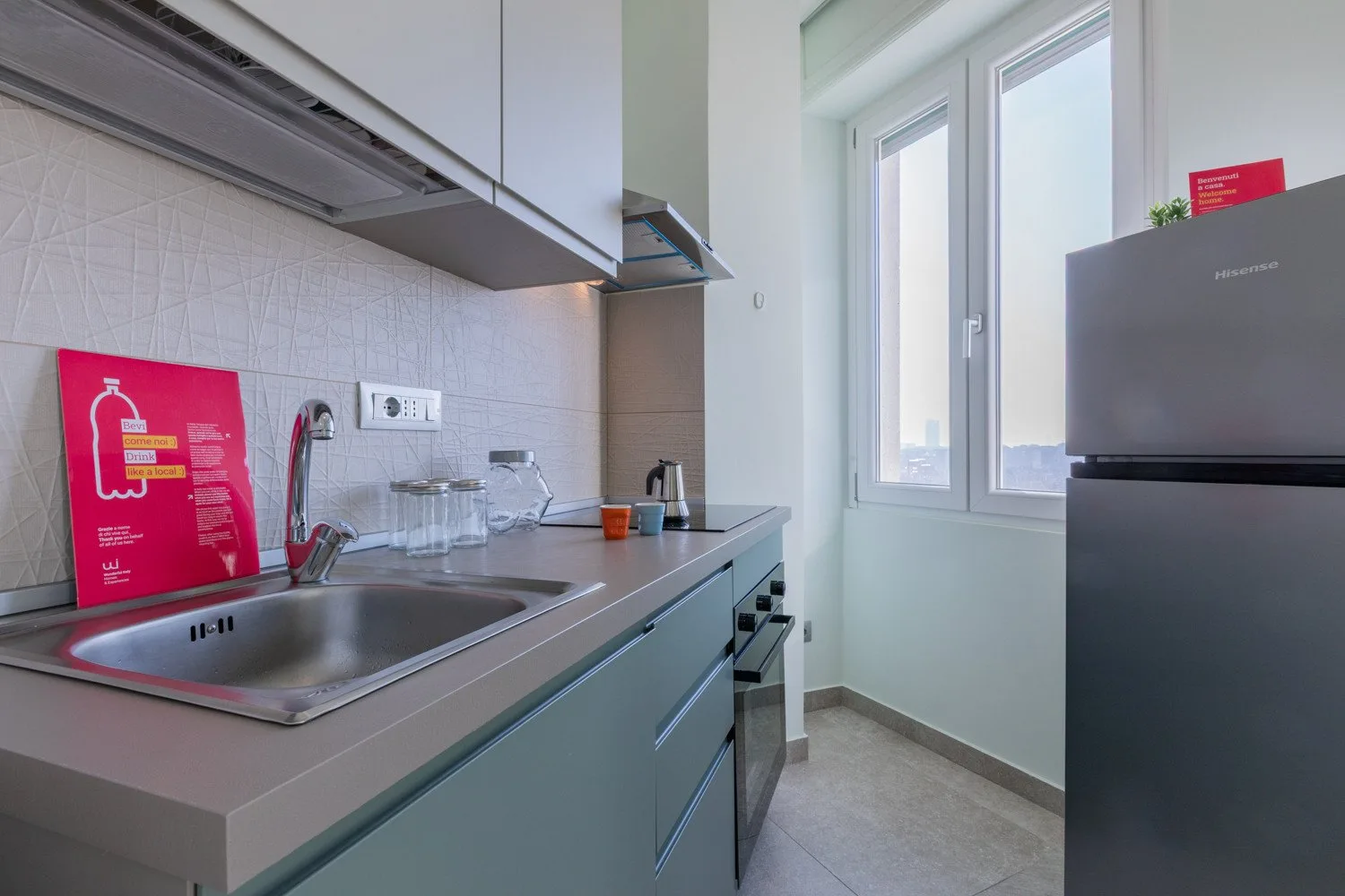 A compact kitchen with a countertop, sink, and tall windows.