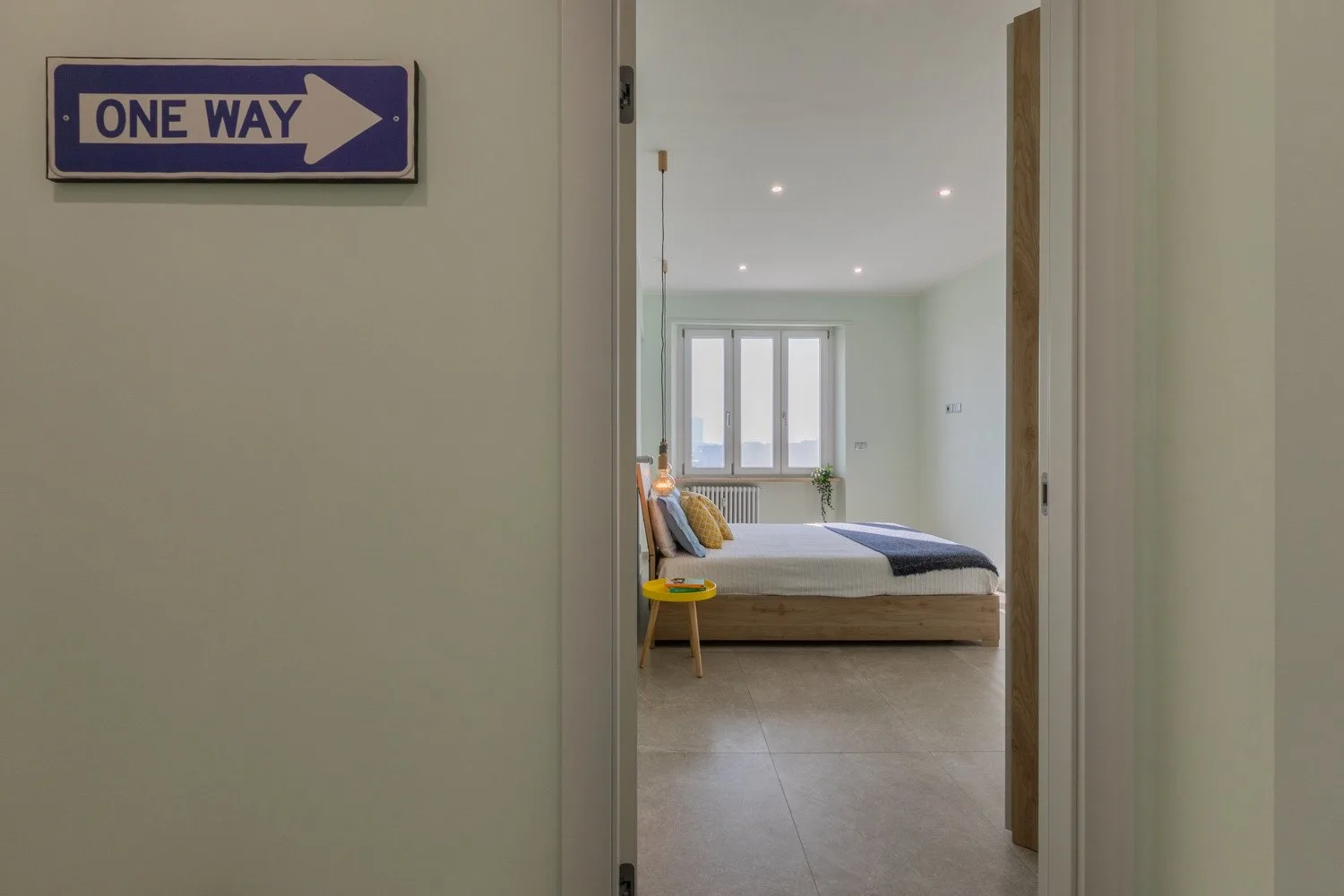 A bedroom is visible through an open doorway, with a bed beneath the windows.