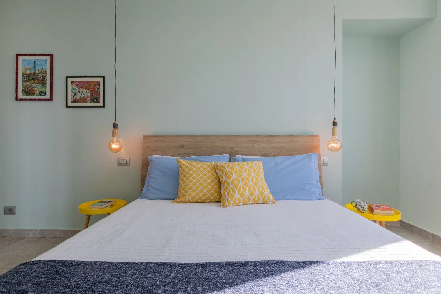 A bedroom with a bed, blue pillows, and two framed pictures on the wall.
