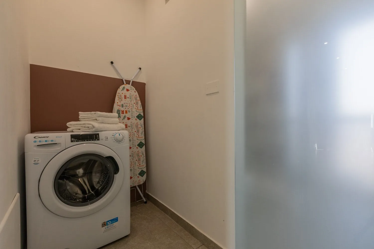 A laundry area with a washing machine, folded towels, and an ironing board.