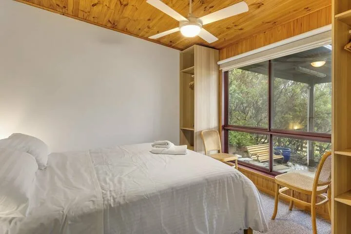Un dormitorio con una cama junto a una ventana grande con vista a los árboles.