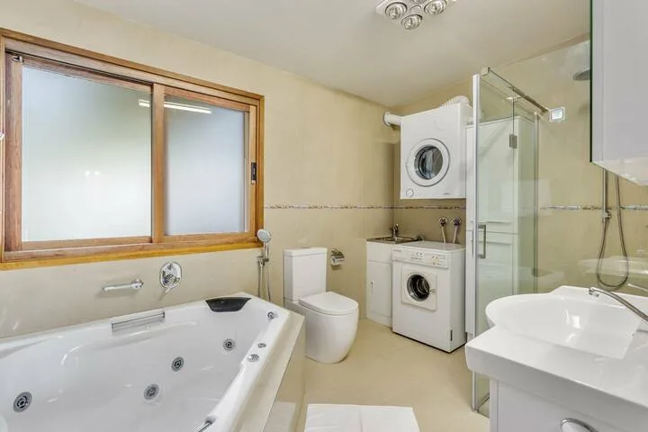 Un baño con bañera, ducha, lavabo y lavadoras.
