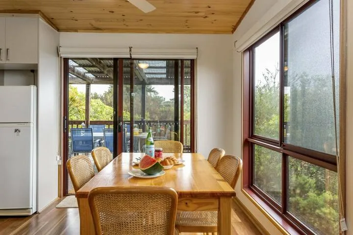Una mesa de comedor de madera con asientos de mimbre está junto a grandes ventanas.