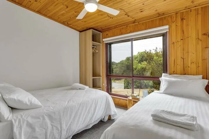 Un dormitorio con dos camas y una gran ventana con vistas a la vegetación.